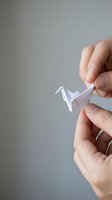Close-up of hands holding delicate white paper crane origami against neutral background. Suitable for concepts of creativity, mindfulness, and craftsmanship.