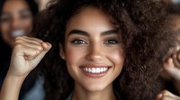 Young African American woman with curly natural hair and bright white smile expressing joy and confidence against blurred background. Positive emotional portrait.
