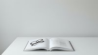 Open book with eyeglasses and pen on white desk, suitable for education, reading, study, and business content.