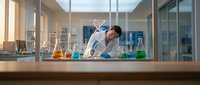 Asian female scientist examining chemical sample in modern laboratory with colorful solutions and glassware for research and development.