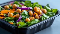 Fresh chickpea salad with baby spinach leaves, sliced carrots, and red onion in black meal prep container. Healthy vegan lunch packed with protein and nutrients.