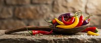 Colorful hot chili peppers in wooden spoon on rustic table with spices. Fresh red yellow peppers for cooking spicy food and seasoning dishes.