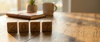 Wooden blocks displaying 2024 numbers on rustic table with coffee mug and notebook in warm morning light for New Year planning and goal setting.