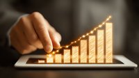 Glowing golden graph chart rising upward on digital tablet screen with finger touch, showing business growth and financial success in dark background.
