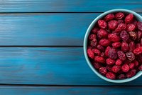 Dried cranberries in white bowl on blue wooden background. Healthy superfood snack rich in antioxidants for cooking, baking and nutrition concepts.
