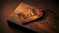 Leather sale tag with embossed text resting on a dark wooden board, warm moody lighting, retail discount and shopping promotion concept.