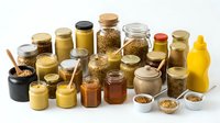 Assorted glass jars and containers filled with various spices, herbs, honey, and condiments arranged on white background for culinary use.