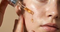 Young woman applying facial serum with dropper for skincare routine. Glowing skin with golden oil drop. Beauty treatment and anti-aging cosmetics concept.