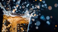 Carbonated cola drink with dynamic splash and fizzy bubbles against dark background with bokeh lights creating refreshing beverage motion photography.