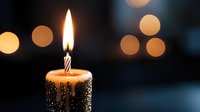 Single lit birthday candle with melting wax against dark background with soft golden bokeh lights creating magical celebratory atmosphere.