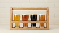 Wooden beer flight tasting set with eight glasses displaying various craft beer styles and colors for brewery sampling and beverage comparison.