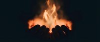 Cupped hands holding bright orange flames against dark background symbolizing power, energy, protection and spiritual connection.
