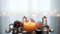 Spa wellness setup with burning candle, healing crystals, gemstones and bokeh lights creating peaceful meditation atmosphere for relaxation therapy.