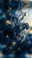 Dark blue ink swirling in water with golden particles creating abstract fluid motion against blurred bokeh background for creative design projects.