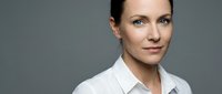 Professional businesswoman in white shirt smiling confidently against gray background for corporate presentations and marketing materials.