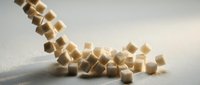 Sugar cubes scattered and stacked on white surface, casting shadows, suitable for food photography, culinary content, and beverage styling.