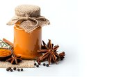 Glass jar with orange honey covered by burlap cloth, decorated with aromatic star anise and black peppercorns on white background, natural food styling.