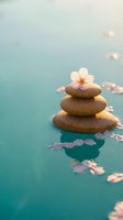 Zen stones balanced in calm turquoise water with floating cherry blossom petals creating peaceful spa atmosphere for meditation and wellness concepts.