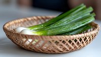 Fresh green onions and white bulbs in traditional woven bamboo basket, shallow depth of field with soft natural lighting, rustic kitchen setting.