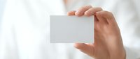 Hand holding blank white business card mockup against soft blurred background for branding and corporate identity design projects.