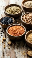 Assorted legumes and grains in wooden bowls on rustic wooden surface, including lentils, chickpeas, and beans for cooking and nutrition.