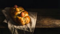 Freshly baked braided challah bread with golden crust on rustic wooden cutting board. Traditional Jewish bakery product for holidays and celebrations.