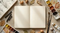 Open blank sketchbook surrounded by watercolor paints, brushes and autumn leaves on wooden surface for artistic creativity and painting projects.