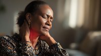 African American woman experiencing neck pain touching sore throat area in home interior setting showing discomfort and health concern symptoms.