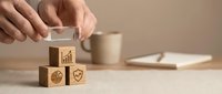Business professional stacking wooden blocks with growth chart, target and shield icons on desk with coffee cup and notebook in modern office workspace.