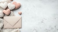 Romantic flat lay with knitted hearts in pink and white colors, beige envelope on marble background. Gentle Valentine's day or love letter concept.