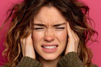 Young woman experiencing severe headache holding temples with pained expression on pink background for health and wellness concepts.
