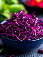 Fresh shredded purple cabbage in dark blue ceramic bowl against black background, macro food photography for healthy eating and recipe blogs.