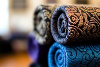 Luxurious rolled fabric with ornate damask pattern in black and turquoise blue, featuring elegant swirls and decorative elements, showcasing rich textile detail.