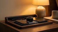 Modern workspace setup with laptop, smartphone, headphones and coffee cup on wooden desk with warm ambient lighting from ceramic table lamp.