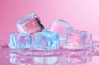 Melting ice cubes with pink and blue reflections on wet surface against pink background create refreshing summer atmosphere for beverage and cooling concepts.