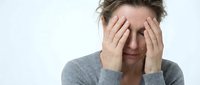 Middle-aged Caucasian woman experiencing headache or stress, holding head in hands wearing gray sweater on white background for health concepts.