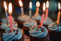 Chocolate cupcakes with blue frosting and colorful lit birthday candles, decorated with sprinkles for celebration party.