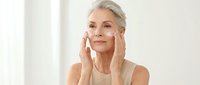 Senior woman applying anti-aging cream to face in bright bathroom. Mature skincare routine, wellness and self-care concept for cosmetic advertising.