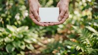 Caucasian male hands holding blank white card against lush green foliage background, suitable for eco-friendly messaging, environmental campaigns, and nature-based branding projects.