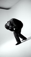 Young man in dark clothing crouched in fetal position showing despair and mental health struggles in minimalist black and white studio setting.