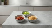 Three ceramic bowls with colorful spices and herbs arranged on modern kitchen counter for cooking and culinary preparation.