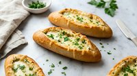 Freshly baked garlic bread slices topped with melted butter, herbs and parsley on white marble surface. Perfect for Italian cuisine and comfort food concepts.