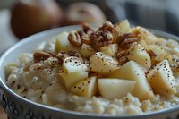 Creamy rice pudding topped with diced pears, pecans and cinnamon spice in white ceramic bowl, comfort food dessert close-up with selective focus.
