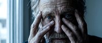 Elderly Caucasian man with hands covering face showing distress, depression or mental health struggles in dramatic lighting by window.