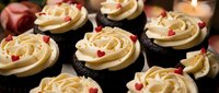 Chocolate cupcakes with vanilla buttercream frosting and red heart sprinkles arranged on dark surface with romantic candle lighting for celebrations.