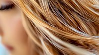 Close up view of blonde highlighted hair strands flowing in gentle waves against soft blurred background, showing natural shine and professional salon styling technique.