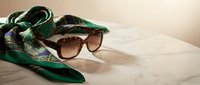 Elegant green silk scarf with paisley pattern and brown sunglasses on marble surface for luxury fashion and accessory styling concepts.