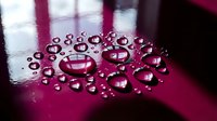 Liquid droplets in various sizes scattered across a vibrant magenta surface with reflective light, suitable for backgrounds, cosmetics, skincare, and wellness product marketing.