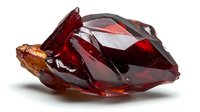 Raw deep red garnet crystal cluster with geometric facets and translucent surfaces showing natural formation and mineral structure on white background.