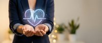 Professional woman in dark blazer holding glowing heart with pulse line hologram, representing healthcare technology and medical innovation in modern office.